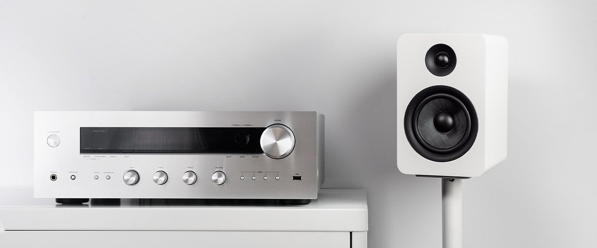 An integrated amplifier sitting on top of a cabinet next to a Kanto YUP6 speaker in white.