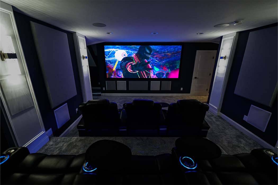 Straight on shot of 7.4.4 home theater with Venom playing on the screen. JL Audio Subwoofers, Revel In-Wall Speakers & JVC NX9 Projector